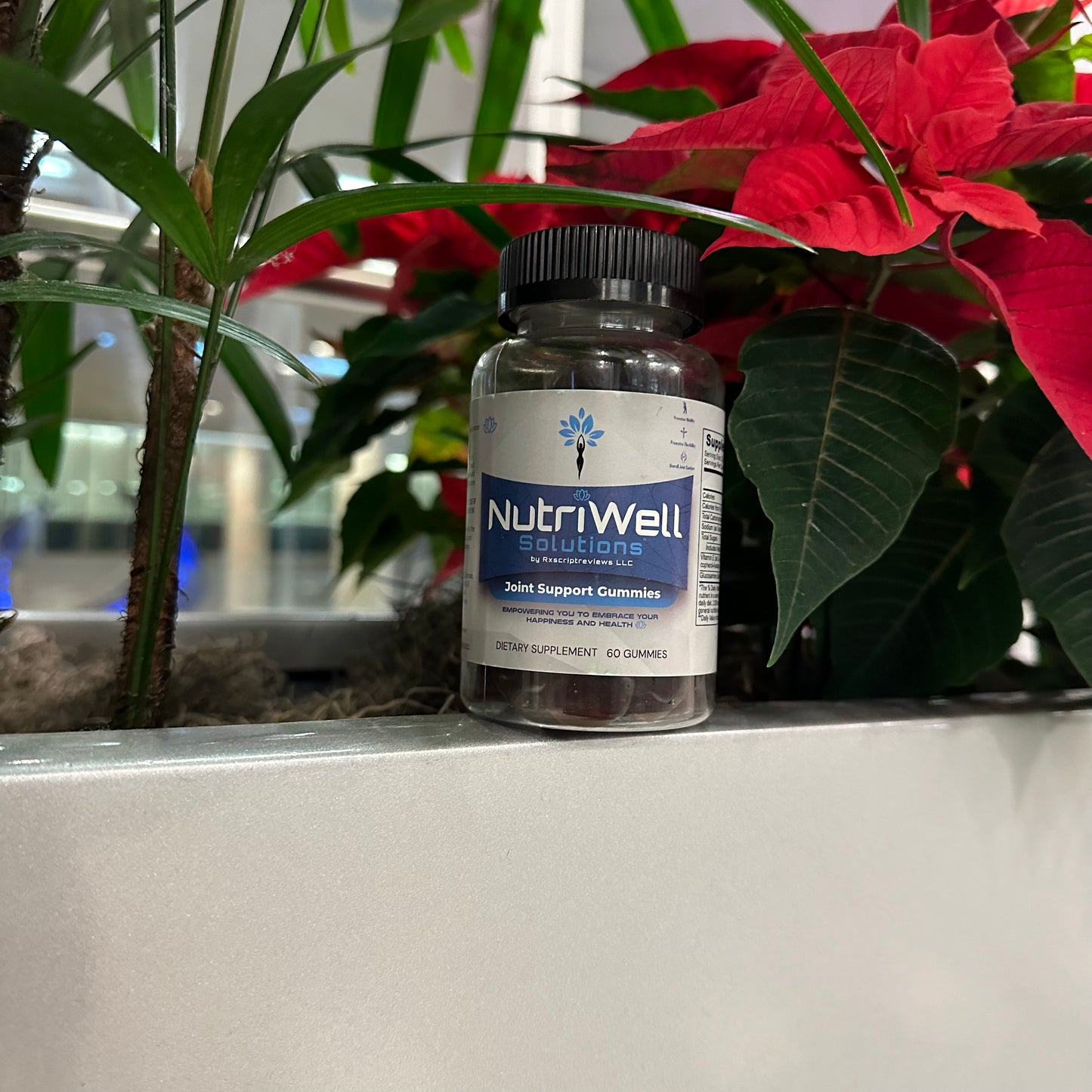 NutriWell Joint Support Gummy Bottle amidst red and green plants at Emory University Hospital, Atlanta, Georgia.